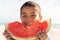 Portrait of smiling cute biracial boy holding large fresh watermelon slice at beach on sunny day