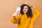 Portrait of a smiling cute curly student woman making selfie photo on smartphone isolated on a beige background