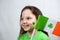 Portrait of smiling endearing small girl in green dress with green shamrock leaf on her cheek and irish flag. Saint Patricks Day