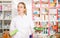 Portrait of smiling friendly female druggist in white coat working in pharmacy