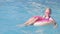 Portrait smiling girl in swimming pool, child in swimming glasses sitting on pink donut swimming ring. Summer travel