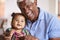 Portrait Of Smiling Grandfather Sitting On Sofa At Home With Baby Granddaughter