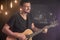 Portrait of smiling guitarist playing acoustic guitar on blurred studio dark background with light bulbs