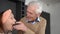 Portrait of smiling handsome senior husband feeding joyful wife with cucumber slice in kitchen at home. Happy loving