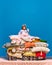 Portrait of smiling, happy little princess sitting on big pile of pillows drink fresh, healthy cocktail over blue