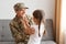 Portrait of smiling happy soldier man wearing camouflage uniform and hat, sitting on cough and talking with his child, daughter