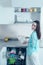 Portrait of a smiling housewife with a clean plate in her hands at an open dishwasher in a white kitchen interior