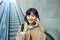 Portrait of smiling korean girl commutes, goes somewhere in city, drinks coffee to go and uses smartphone, stands on