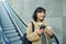 Portrait of smiling korean girl commutes, goes somewhere in city, drinks coffee to go and uses smartphone, stands on