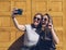 Portrait of a smiling lesbian young couple posing for a selfie in a yellow door. Happiness and joyful lifestyle concept