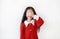 Portrait of smiling little Asian child girl in scarlet red dress covering eyes with hand isolated over white background