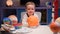 Portrait smiling little blond boy sitting at home at table near planet Sun around many planets of solar system. Child