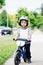 Portrait of smiling little boy toddler riding a balance bike bicycle in helmet on the road outside outdoors on spring summer day