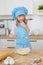 Portrait of a smiling little girl in a cook clothes tests a dough in a bowl