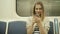 Portrait of a smiling lovely girl typing message on mobile phone in subway train, student blonde woman with