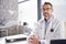 Portrait Of Smiling Male Doctor Wearing White Coat With Stethoscope Sitting Behind Desk In Office