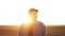 Portrait of smiling male farmer in cap is walking through endless plowed farmland field on sunset. Professional