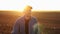 Portrait of smiling male farmer in cap is walking through endless plowed farmland field on sunset. Professional