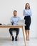 Portrait Of Smiling Man Sitting At Desk, Woman Standing