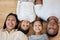 Portrait of smiling mixed race family of four from above lying and relaxing on wooden floor at home. Carefree loving