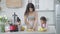 Portrait of smiling mother slicing fruits with knife on cutting board in kitchen as children waiting for healthy tasty