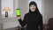 Portrait of smiling muslim woman in hijab holding smartphone with green screen. Modern eastern lady in black clothes