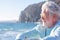 Portrait of smiling pensive senior man white haired sitting at the beach looking the horizon over sea. Elderly enjoying summer