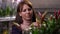 Portrait of smiling positive Caucasian woman admiring flower stem in flower shop indoors. Happy confident buyer choosing