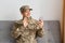 Portrait of smiling positive military man wearing camouflage uniform sitting on sofa, soldier talking on video call, saying hello