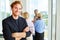 Portrait of smiling redhead businessman standing with arms crossed against team discussing at workplace