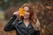 Portrait of smiling redhead woman with yellow leaf with long curly hair on blurred autumn background. Girl on fabulous background