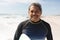 Portrait of smiling retired biracial senior man standing with surfboard at beach on sunny day