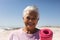 Portrait of smiling retired biracial senior woman holding exercise mat with short hair at beach