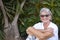 Portrait of a smiling retired white-haired woman sitting and relaxed in a public park near palm trees. Attractive senior people