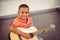 Portrait of smiling schoolboy playing guitar in classroom