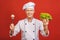 Portrait of a smiling senior chef cook holding salad and mushroom isolated on a red background