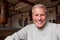 Portrait Of Smiling Senior Male Boxing Coach In Gym Standing By Old Fashioned Leather Punching Bags