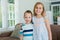 Portrait of smiling sister and brother standing with arms around in living room