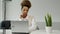 Portrait of a smiling, thoughtful woman sitting at an office desk with a laptop