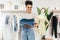 Portrait of a smiling woman in her small clothing retail shop. Happy business owner holding a pile of clothing and looking away