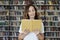 Portrait of smiling woman model reading text with opened book in a library, bookshelf behind, long hair. Hipster college student