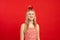 Portrait of smiling wonderful teenage girl with fair hair holding balancing big red apple on head on red background.