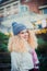 Portrait of smiling young curly blond woman in warm white natural sweater and blue knitted beanie hat with pompom looking at