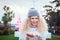Portrait of smiling young curly blond woman in warm white sweater and blue knitted beanie hat with pompom holding gift box in
