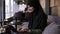 Portrait of smiling young muslim woman working on modern laptop in cafe. Attractive woman in hijab opens the laptop and