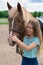 Portrait of smiling young woman with blond long hair is caressing brown horse snoot with big nostrils. Horseback riding hobby, vac