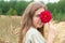 Portrait of smiling young woman looking at camera holding delicate red dahlia flower and covering her eye with it.