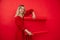 Portrait of smiling young woman in red outfit uncovering red empty whatman paper isolated on red background. Marketing