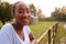 Portrait Of Smiling Young Woman Taking A Break And Resting On Fence During Walk In Countryside