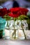 A portrait of some red roses standing on a wooden table in some glass bottles. The flowers are starting to bloom